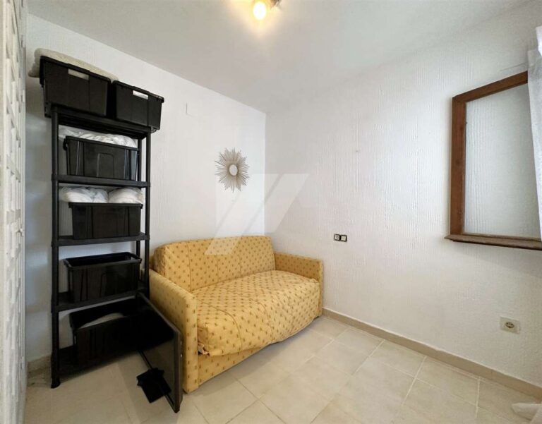 Second bedroom inside a single-level villa near El Portet Beach in Moraira with sofa bed, shelving, window and simple neutral finish