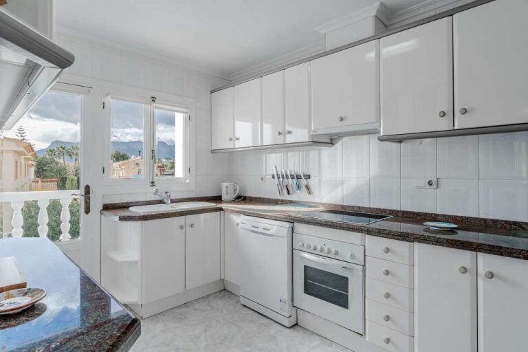 Separate fitted kitchen with white cabinets inside a Mediterranean villa with guest accommodation in Calpe.