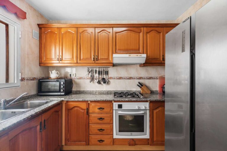 Separate fitted kitchen with wooden cabinets inside a single-level villa in Calpe close to beaches and amenities.