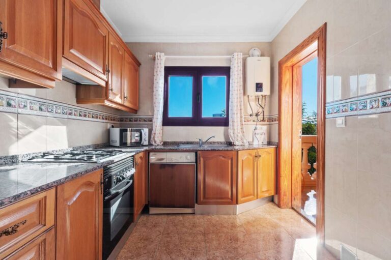 Separate kitchen with wooden cabinets and fitted appliances inside a guest apartment at a spacious villa in Calpe.