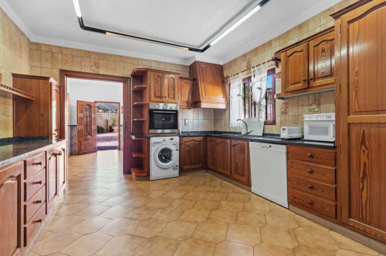 Separate kitchen with wooden cabinets and fitted appliances inside a spacious villa with guest apartments in Calpe.