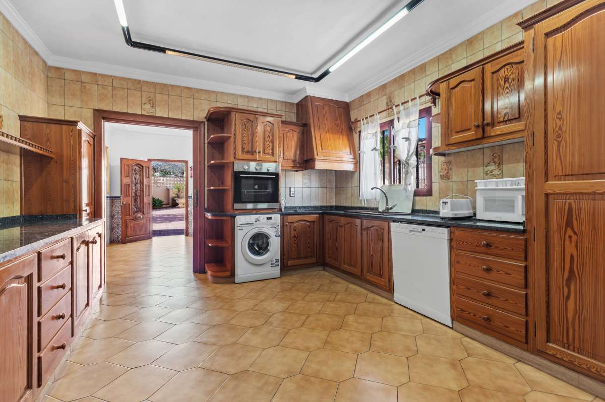 Separate kitchen with wooden cabinets and fitted appliances inside a spacious villa with guest apartments in Calpe.