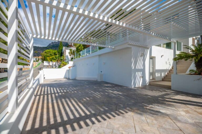 Shaded exterior terrace at a modern villa in Altea Hills with pergola, paved outdoor area, white walls and garden access