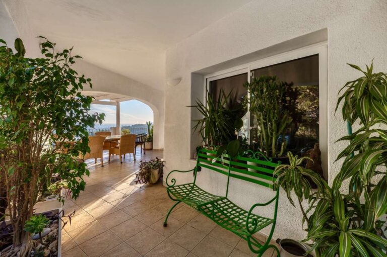 Shaded terrace seating area at a Benissa sea view villa with green bench, Mediterranean plants and covered outdoor space