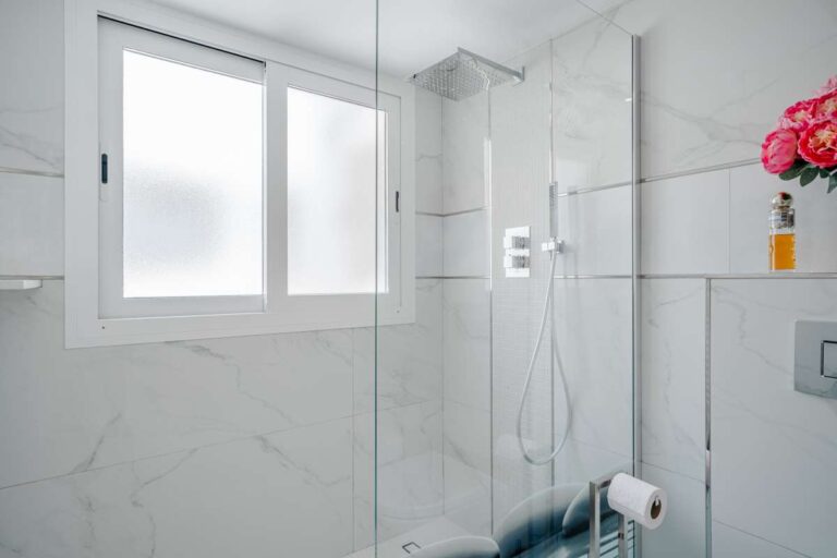 Shower area inside a renovated Arenal-Bol apartment in Calpe with white tiled finish, window and modern bathroom fittings