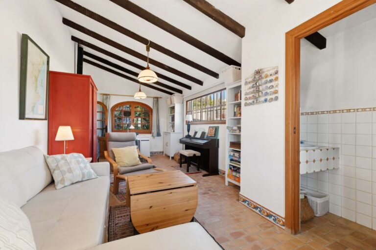 Sitting room inside a traditional Spanish finca near Moraira with beamed ceiling, sofa seating, bathroom access and rustic interior details