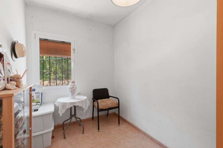 Small bedroom inside a Mediterranean villa in Benissa Costa near Cala Baladrar with window, chair and simple bright interior layout