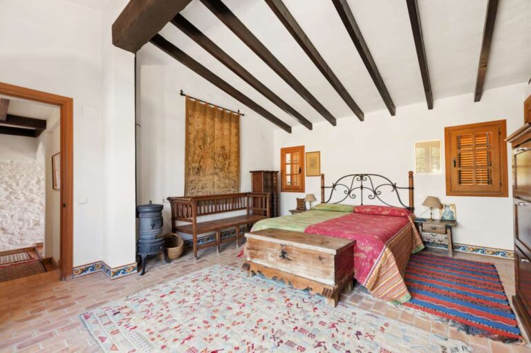 Spacious bedroom inside a traditional Spanish finca near Moraira with beamed ceiling, wooden bed, tiled floor and rustic Mediterranean character