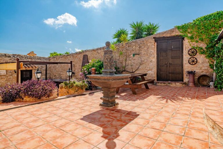 Spacious courtyard at a historic finca in Benissa with stone walls, traditional fountain, terracotta flooring and Mediterranean planting