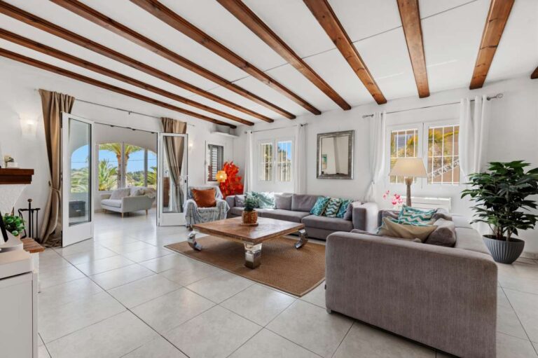 Spacious living room inside a renovated single-level villa in Moraira with beamed ceiling, sofa seating, fireplace and terrace access