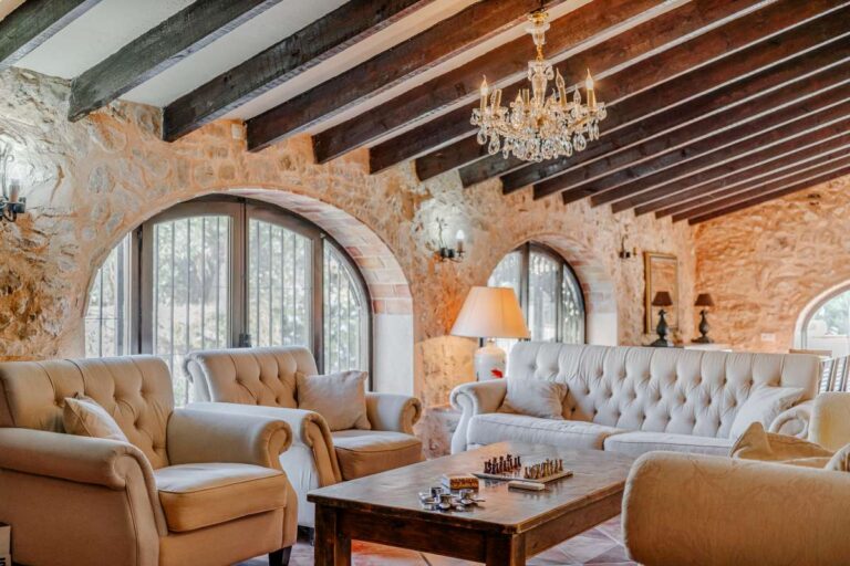 Stone living room inside a historic luxury finca in Benissa with wooden beams, arched windows, chandelier and classic seating area