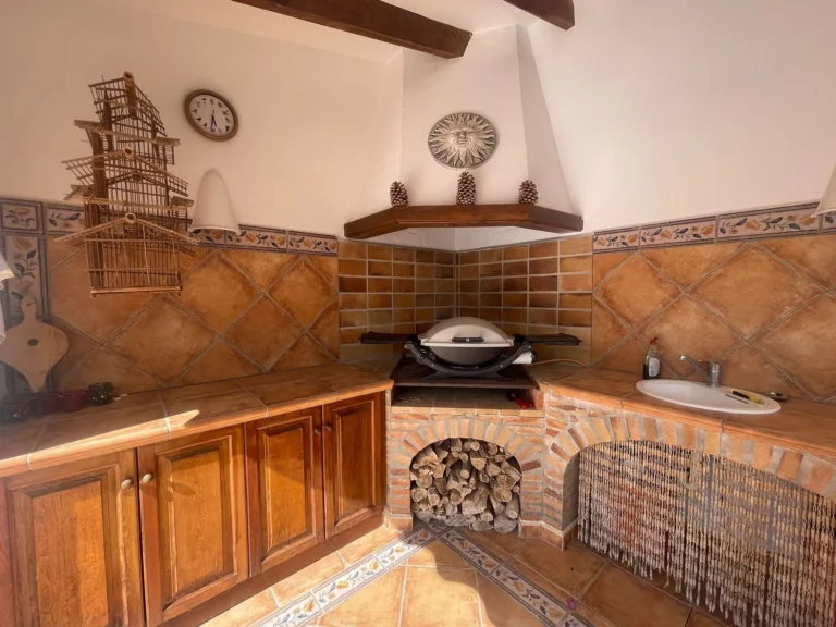 Summer kitchen with BBQ area, sink, tiled worktops, and wood storage at a villa in Calpe.