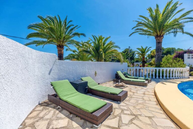 Sun loungers beside the private pool at a renovated single-level villa in Moraira with palm trees, stone terrace and Mediterranean garden setting
