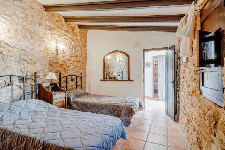 Traditional bedroom inside a historic luxury finca in Benissa with stone walls, wooden beams, twin beds and Mediterranean character