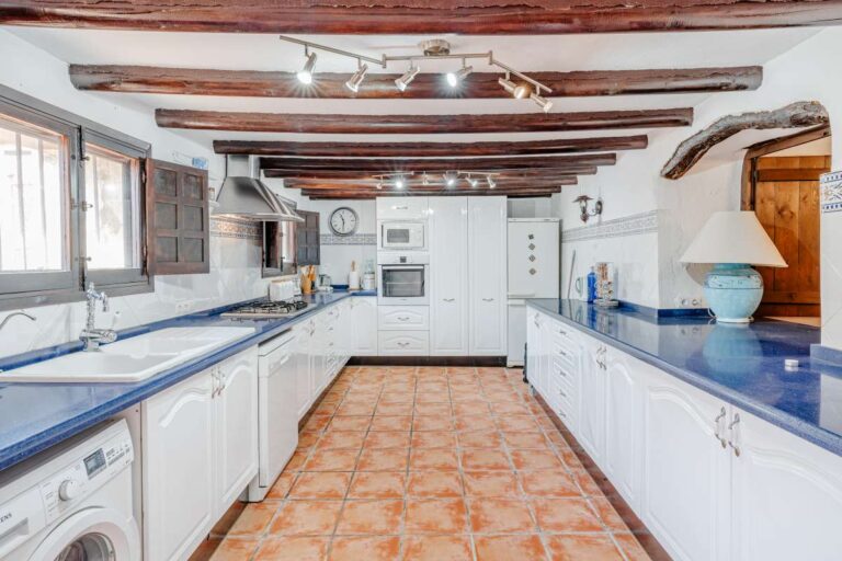 Traditional kitchen inside a historic finca in Benissa with wooden beams, white cabinetry, tiled flooring and rustic Mediterranean character