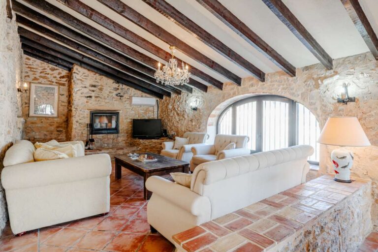 Traditional lounge inside a historic finca in Benissa with stone walls, wooden beams, fireplace and classic Mediterranean character