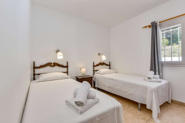 Twin bedroom inside a charming Benissa Coast villa with two single beds, bedside table, window and bright neutral finish