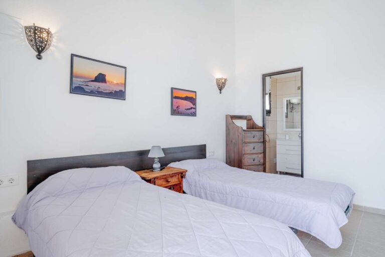 Twin bedroom inside a historic finca in Benissa with bright white walls, traditional furniture and en-suite bathroom access