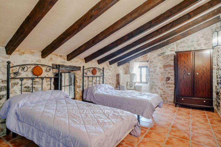Twin bedroom inside a historic finca in Benissa with stone walls, wooden beams, traditional tiled flooring and rustic Mediterranean character