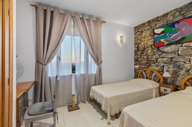 Twin bedroom inside an independent apartment of a Benissa sea view villa with stone feature wall, window, curtains and traditional furniture