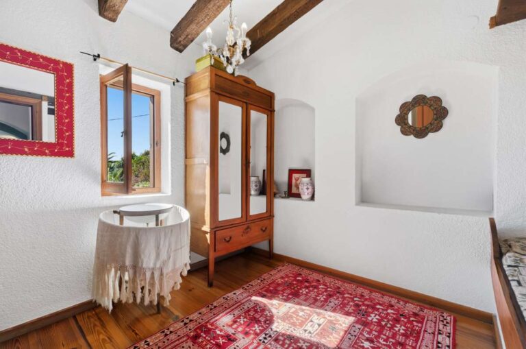 Upper bedroom inside a traditional Spanish finca near Moraira with beamed ceiling, wooden wardrobe, window, rug and rustic Mediterranean details