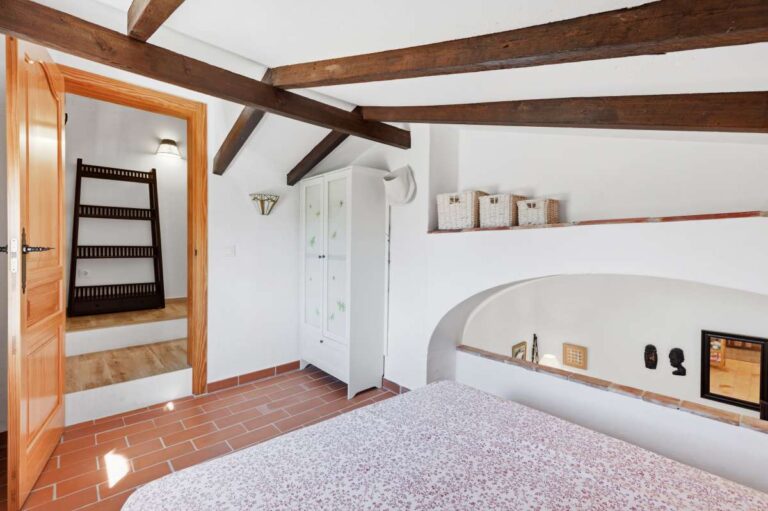 Upper bedroom inside the guest house of a traditional Spanish finca near Moraira with beamed ceiling, staircase access, air conditioning and rustic interior details