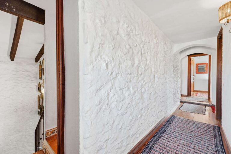 Upper hallway inside a traditional Spanish finca near Moraira with textured white walls, beamed ceiling, tiled floor and rustic Mediterranean character