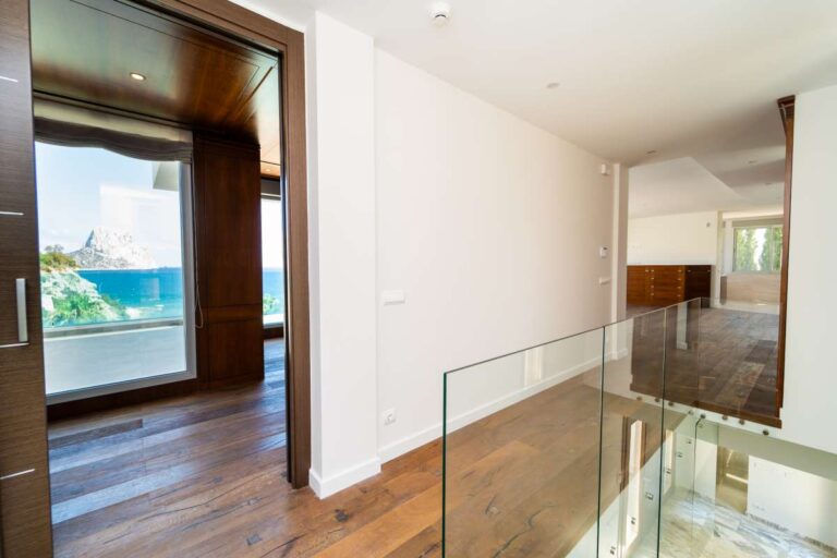 Upper landing inside a luxury villa in Calpe with wood flooring, glass balustrade and sea views through large windows