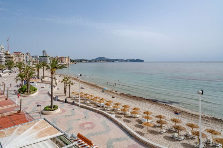 Views from a beachfront apartment by La Fossa Beach in Calpe showing the promenade, sunbed area, sandy beach and calm bay