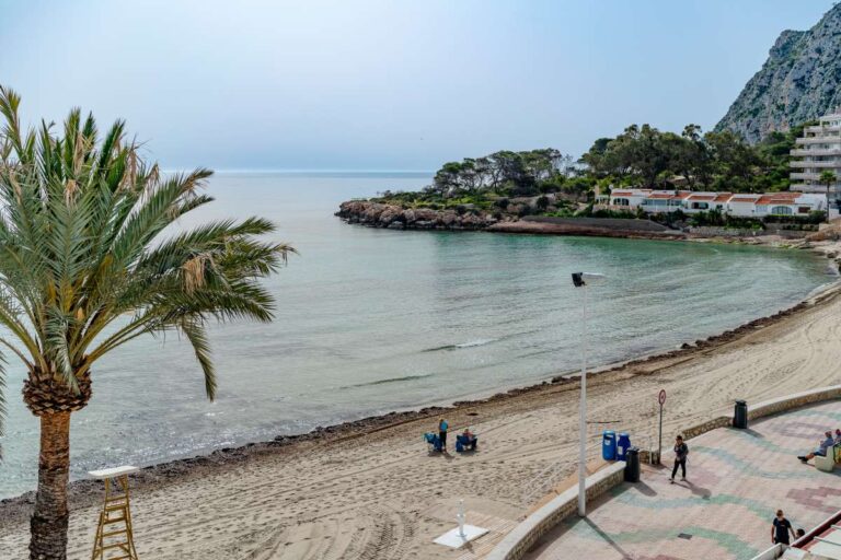 Views from a beachfront apartment by La Fossa Beach in Calpe showing the sandy beach, palm tree, rocky coastline and Mediterranean Sea