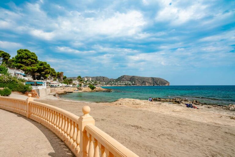 Views of Les Platgetes Beach in Moraira with Mediterranean Sea, coastal walkway, sandy beach and surrounding shoreline