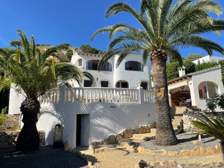 White villa exterior with palm trees, stone landscaping, and garden terraces in Calpe.