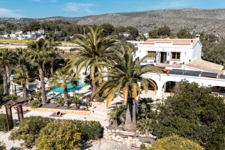 Aerial view of a renovated finca near Teulada and Moraira with palm trees, swimming pool, landscaped gardens and surrounding countryside