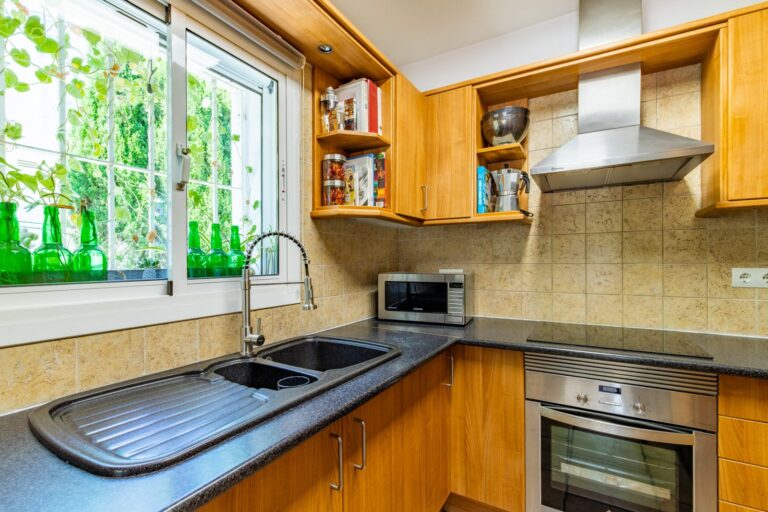 Alt text: Fully equipped kitchen inside a Mediterranean villa near Cala Baladrar in Benissa Costa with wooden cabinetry, built-in oven, window and practical layout