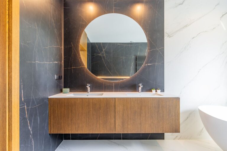 Bathroom inside a luxury smart home villa near Moraira with double vanity, round mirror, warm lighting, black wall finish and premium contemporary design