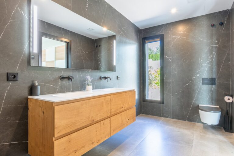 Bathroom inside a modern villa in Solpark, Moraira with double vanity, wooden cabinetry, large mirror, dark tiled walls and modern fittings