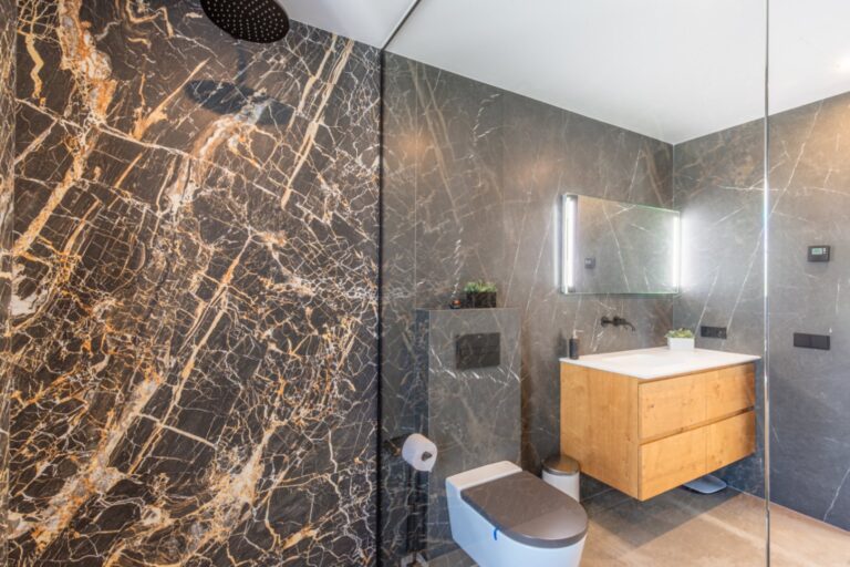 Bathroom inside a modern villa in Solpark, Moraira with walk-in shower, dark marble-effect wall tiles, wooden vanity and contemporary fittings