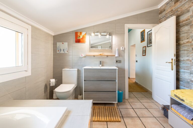 Bathroom inside a renovated finca near Teulada and Moraira with vanity unit, bathtub, toilet, bright window and natural stone wall detail