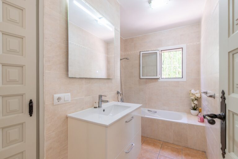 Bathroom inside a renovated Mediterranean villa in Moraira with bathtub, vanity unit, large mirror, bright window and neutral tiled finish