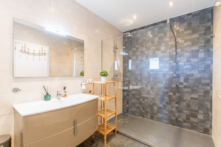 Bathroom inside a renovated Mediterranean villa in Moraira with walk-in shower, vanity unit, large mirror and dark feature wall tiles