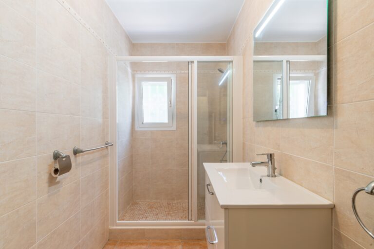 Bathroom inside a renovated Mediterranean villa in Moraira with walk-in shower, vanity unit, large mirror, bright window and neutral tiled finish