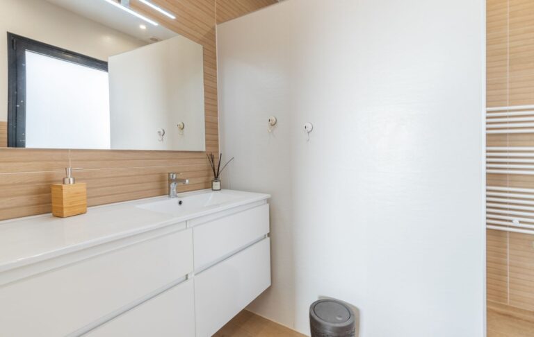 Bathroom vanity inside a modern villa in Pla del Mar, Moraira with white cabinetry, large mirror, towel rail and contemporary finish