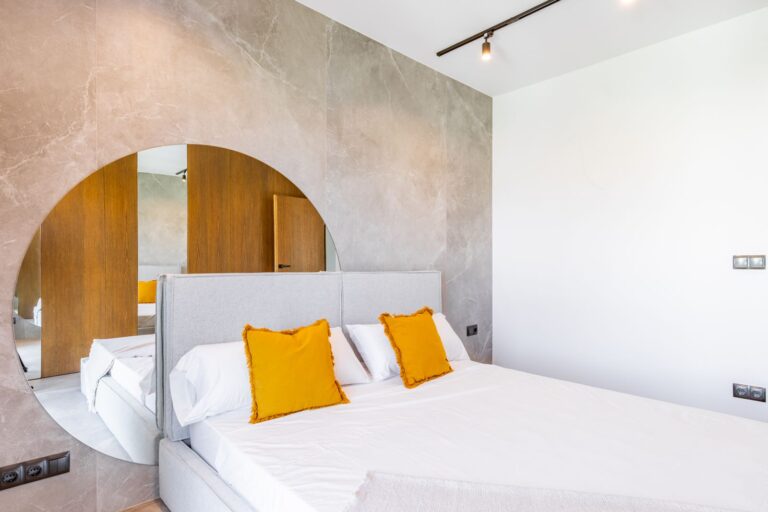Bedroom inside a luxury smart home villa near Moraira with round mirror feature wall, white bed, warm wood finishes and premium contemporary design