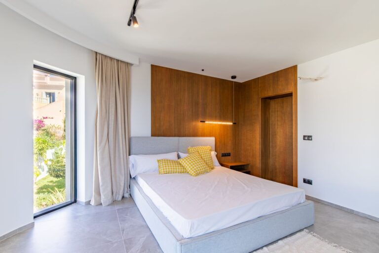Bedroom inside a luxury smart home villa near Moraira with terrace access, fitted wooden wardrobes, large window, white bed and warm contemporary finish