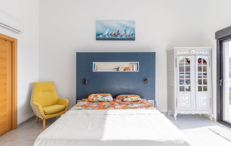 Bedroom inside a modern villa in Pla del Mar, Moraira with double bed, yellow armchair, fitted storage, large window and bright contemporary interior