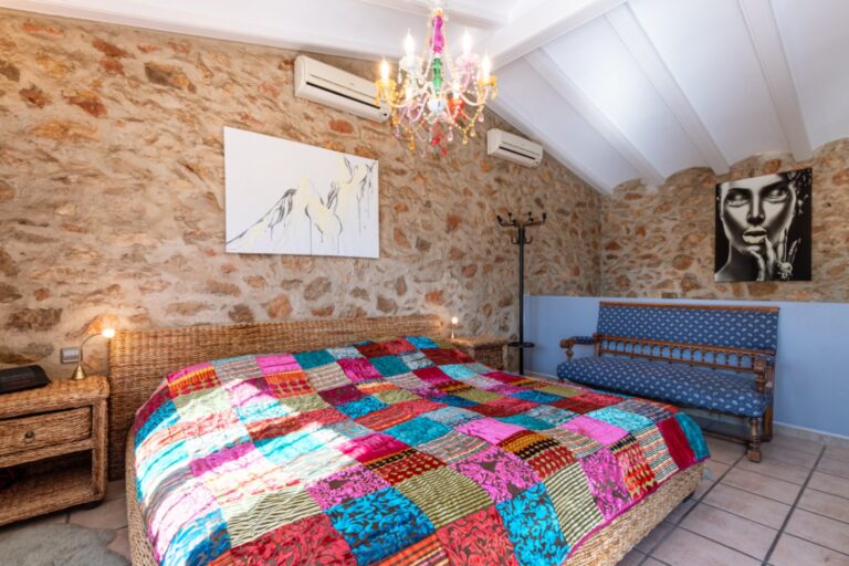 Bedroom inside a renovated finca near Teulada and Moraira with stone feature wall, double bed, beamed ceiling, air conditioning and warm character details