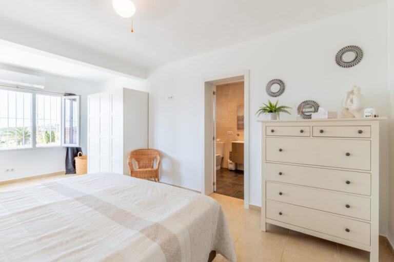 Bedroom inside a renovated Mediterranean villa in Moraira with double bed, dresser, en-suite access, bright windows and neutral finish
