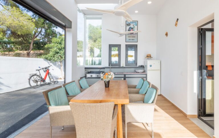 Covered dining area at a modern villa in Pla del Mar, Moraira with wooden table, terrace access, contemporary exterior and garden views