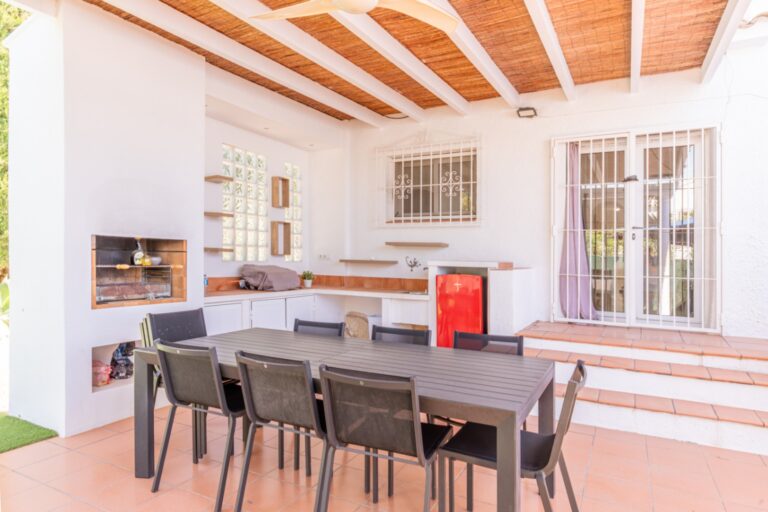 Covered outdoor dining area at a renovated Mediterranean villa in Moraira with dining table, built-in barbecue, timber ceiling and terrace access
