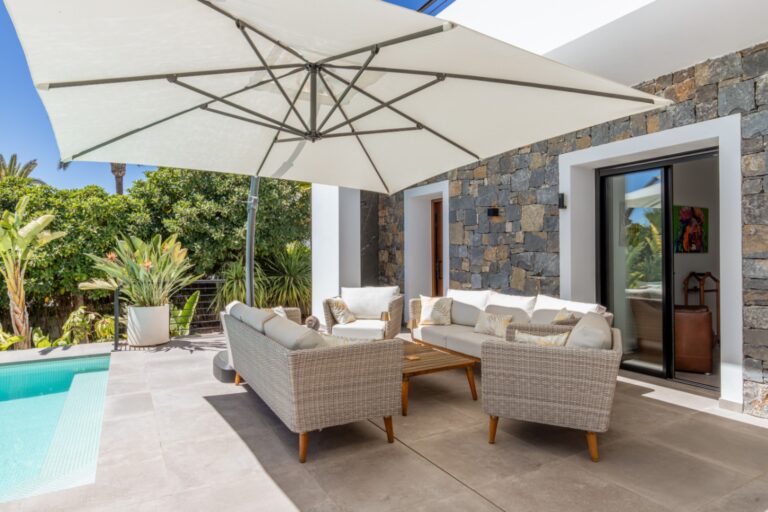 Covered outdoor lounge area at a modern villa in Solpark, Moraira with sofa seating, parasol, pool terrace and landscaped garden surroundings
